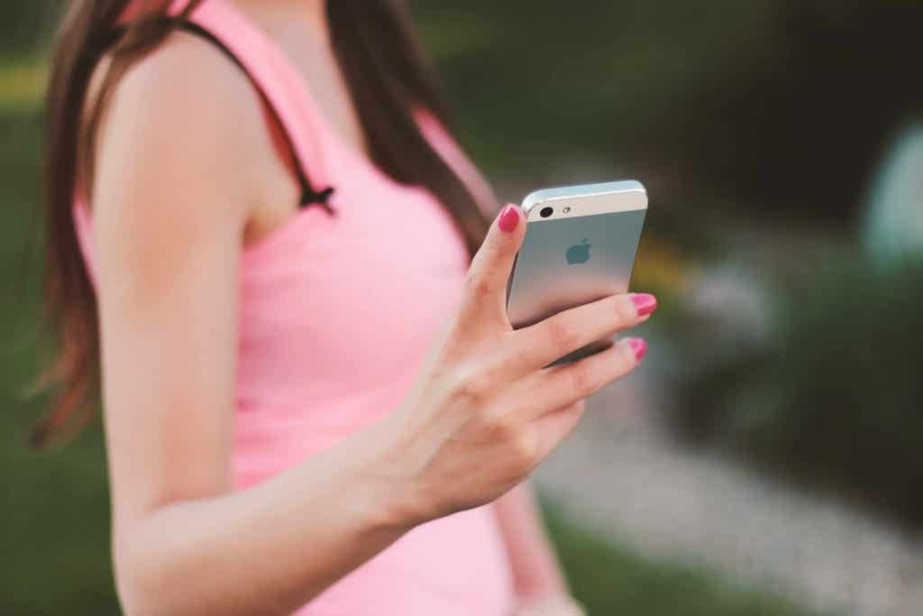 Zdjęcie przedstawia kobietę w różowej sukience trzymającą telefon komórkowy.