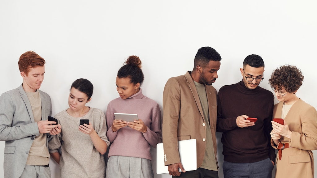 Grafika, przedstawiająca grupę osób wpatrującą się w ekrany swoich telefonów komórkowych.